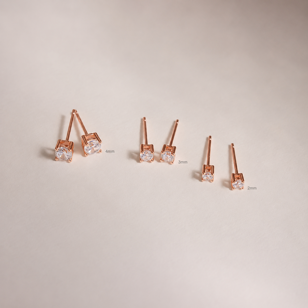 Set of rose gold earrings with clear gemstones on a beige background
