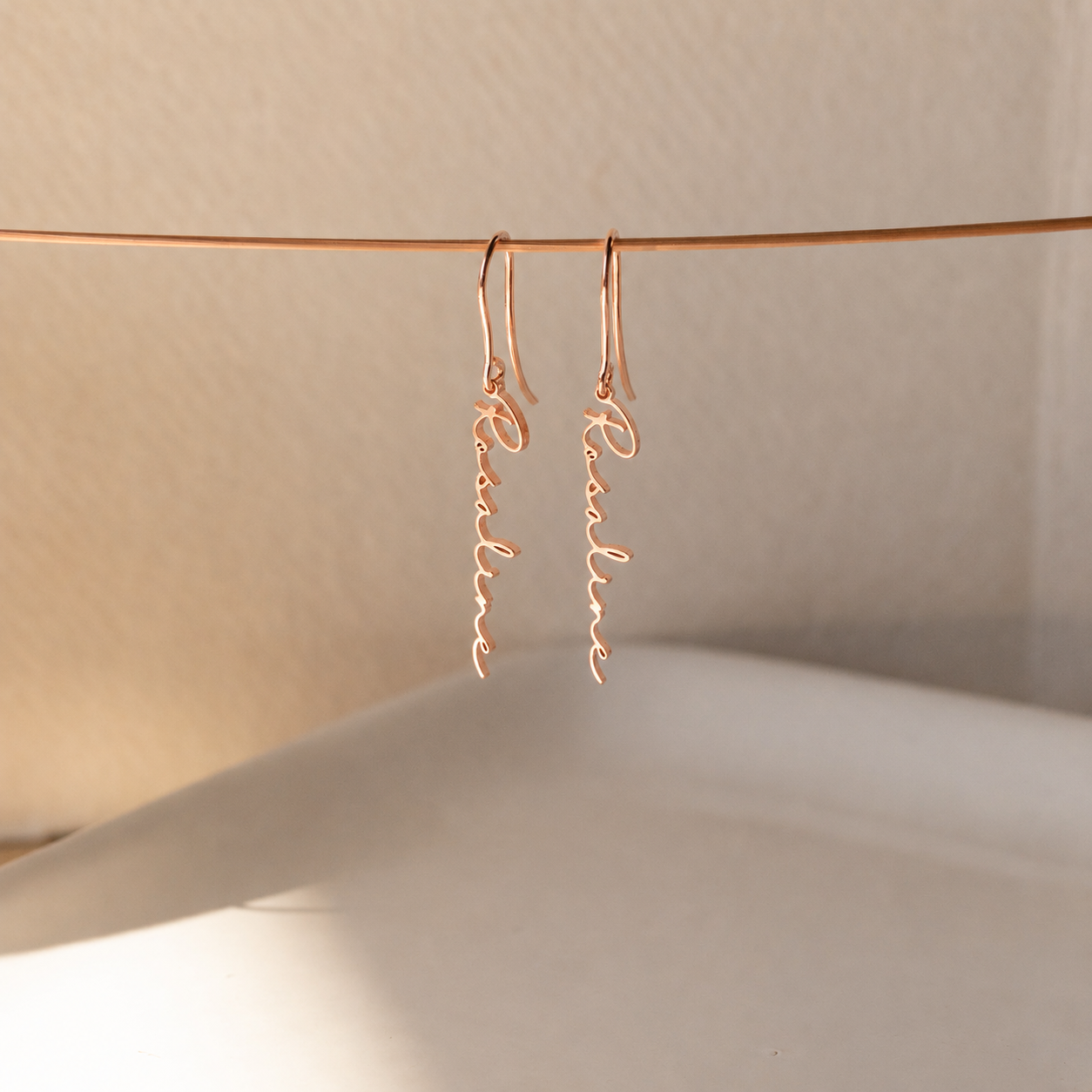 Rose gold earrings with 'Renee' on a neutral background