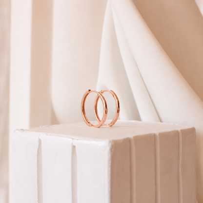 Rose gold hoop earrings on a white pedestal with a soft beige background