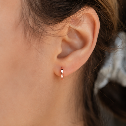 Close-up of an ear wearing a rose gold hoop earring with blurred background