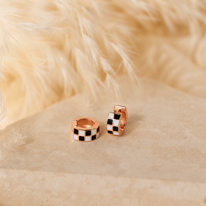 Pair of rose gold hoop earrings with black and white checkered pattern on a beige fur background