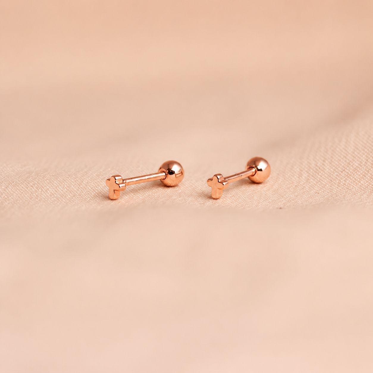 Rose gold bar-shaped earrings on a beige fabric background