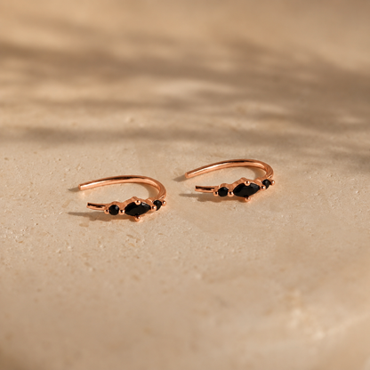 Rose gold open rings with black gemstones on a beige surface