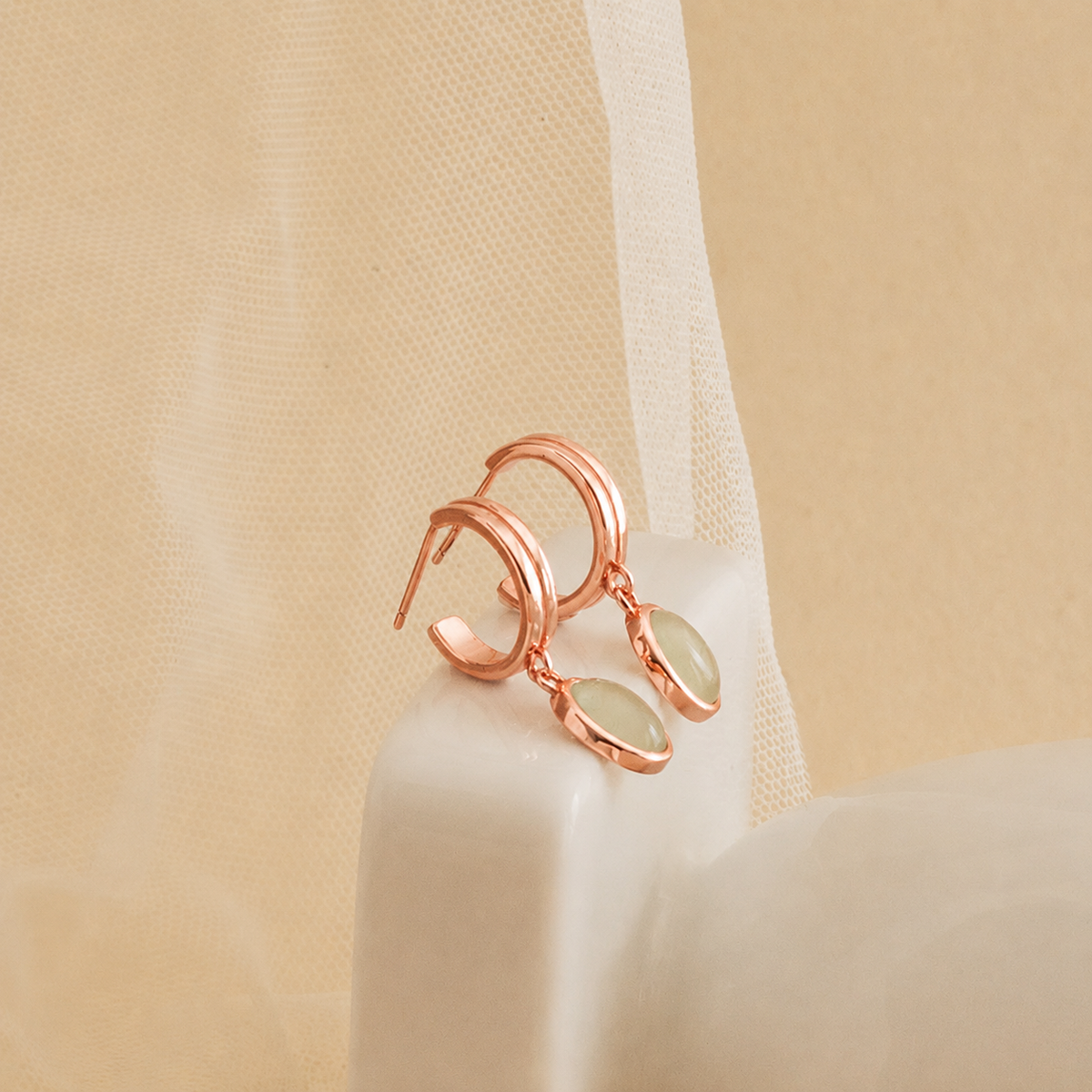 Rose gold earrings with green gemstones on a beige fabric background