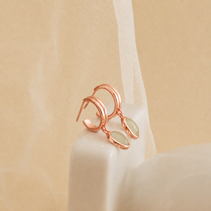Rose gold earrings with green gemstones on a beige fabric background