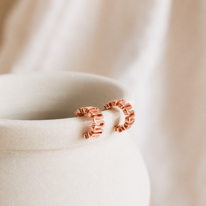 Rose gold hoop earrings on a beige fabric background