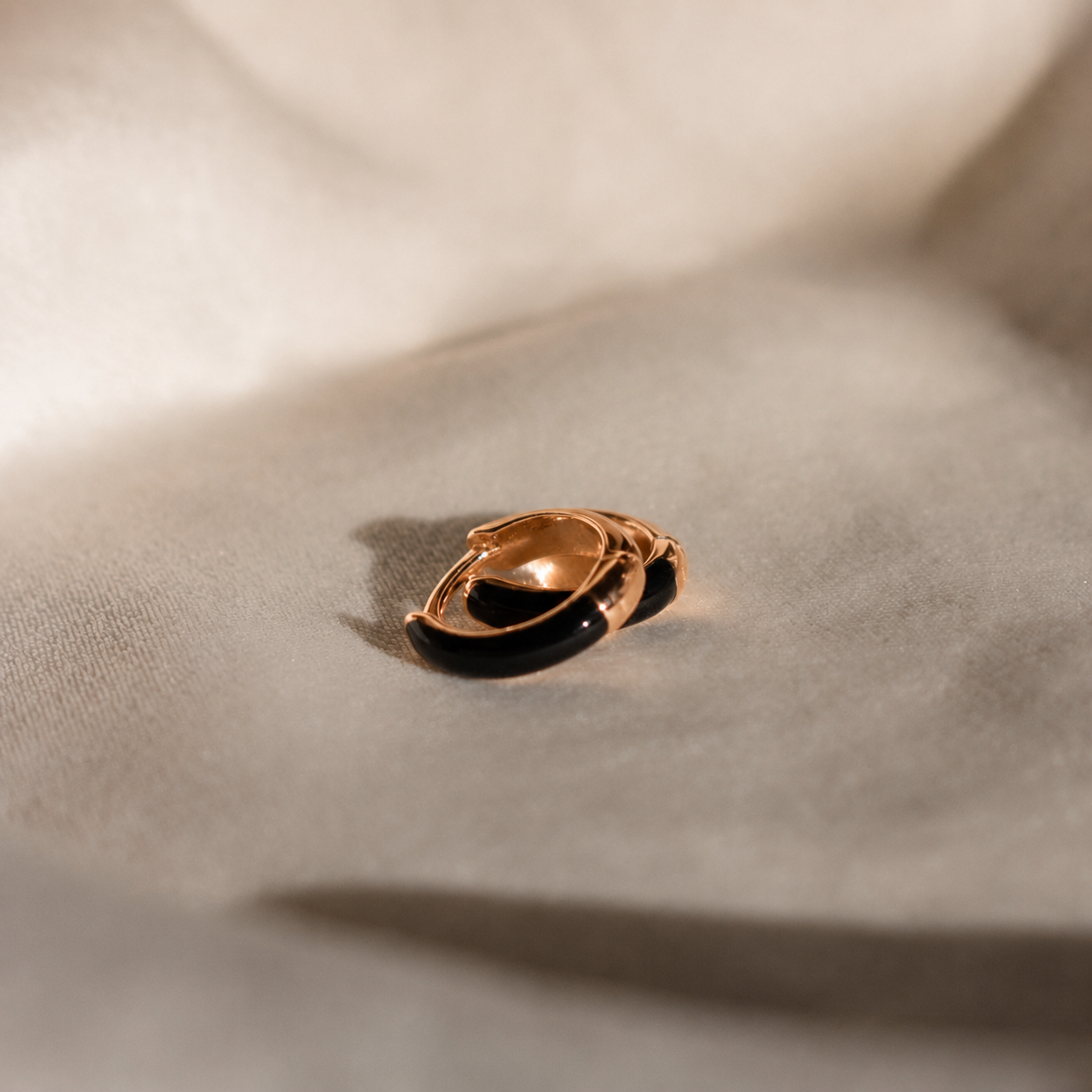 A gold ring with a black inlay, photographed on draped beige fabric with soft shadows.