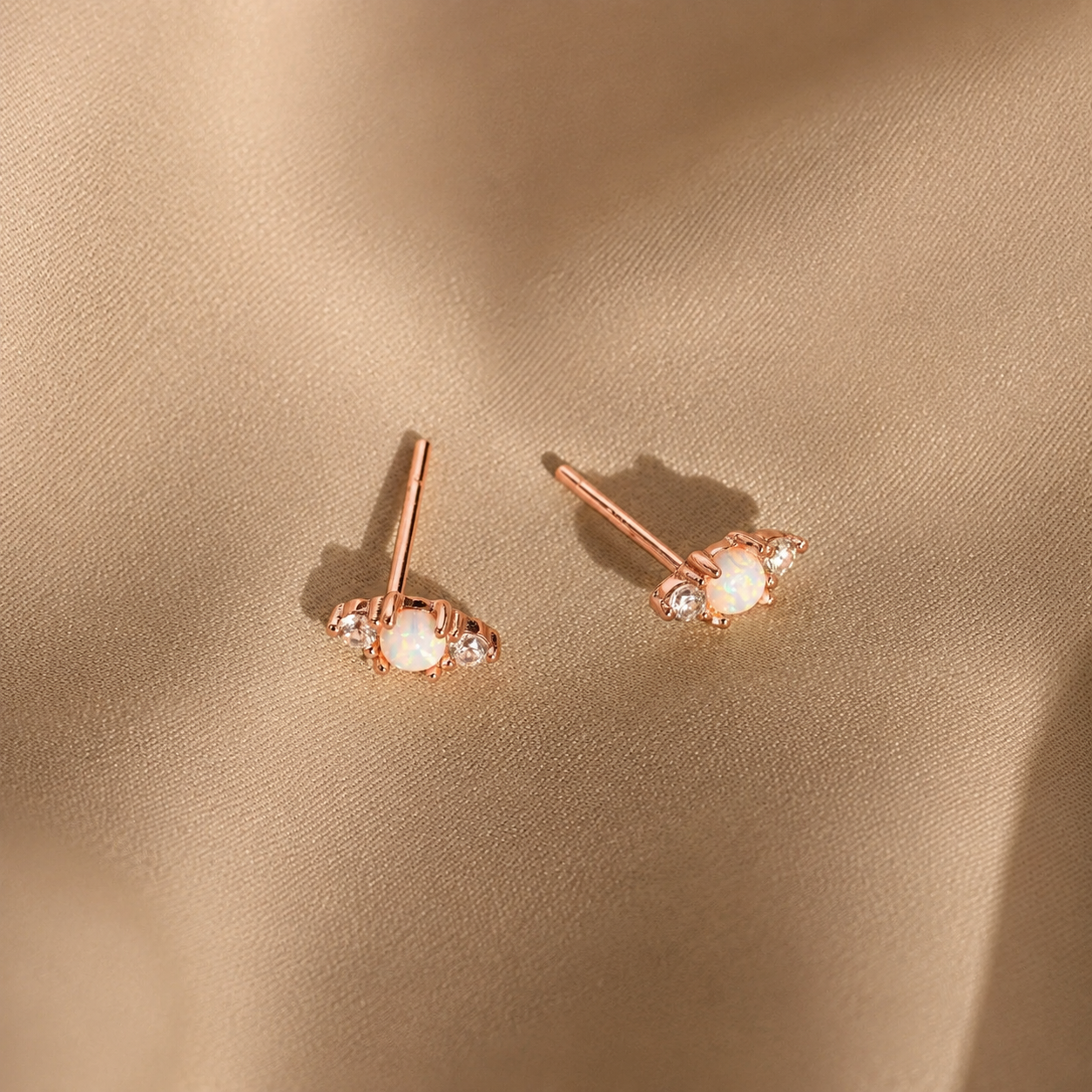 Rose gold earrings with gemstones on a beige fabric background