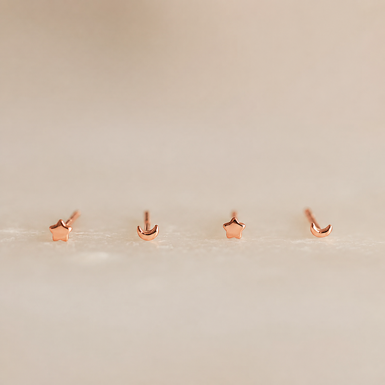Set of rose gold star and moon earrings on a light beige background