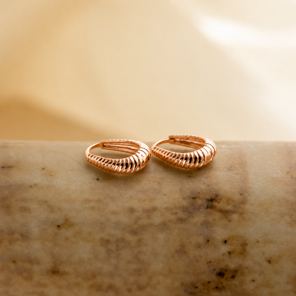 Pair of rose gold hoop earrings on a textured beige surface