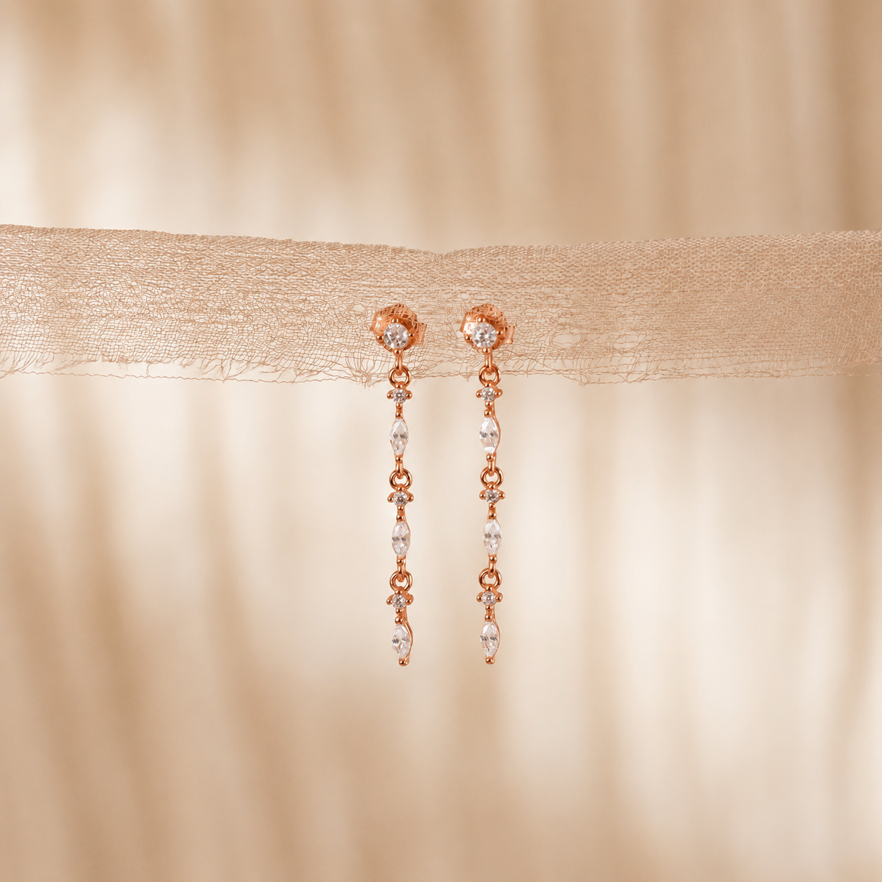 Rose gold earrings with clear gemstones on a beige fabric background