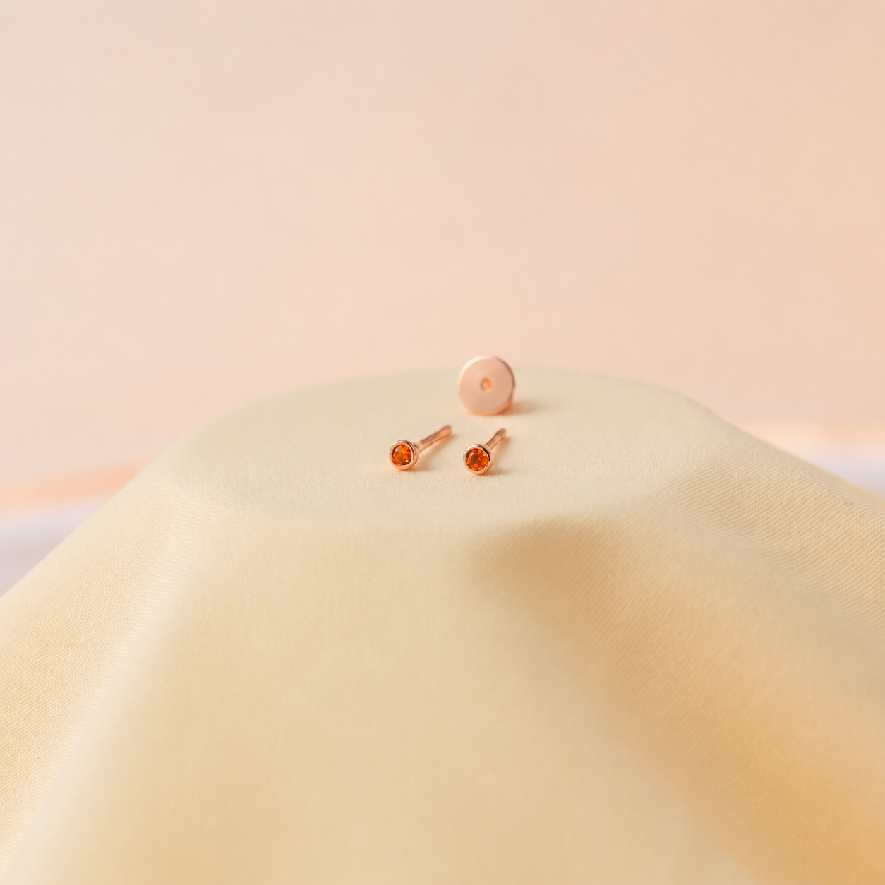 Pair of rose gold earrings with orange gemstones on a soft beige background