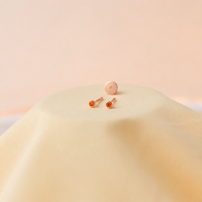 Pair of rose gold earrings with orange gemstones on a soft beige background
