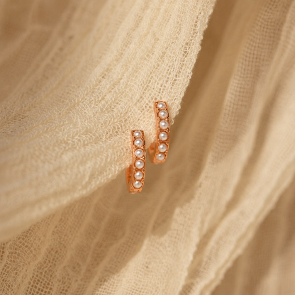 Rose gold hoop earrings with embedded stones on beige fabric
