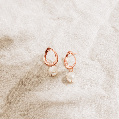 Rose gold earrings with pearl drops on a textured beige fabric background