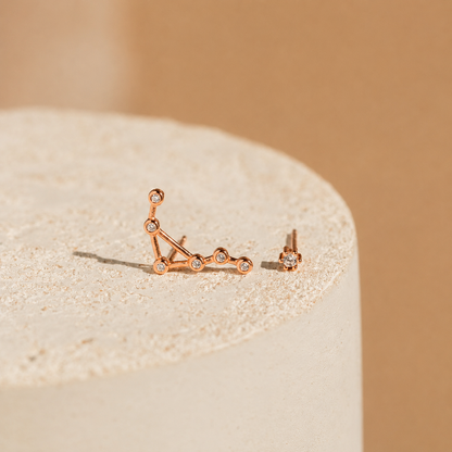 Rose gold constellation earrings on a beige stone with a beige background