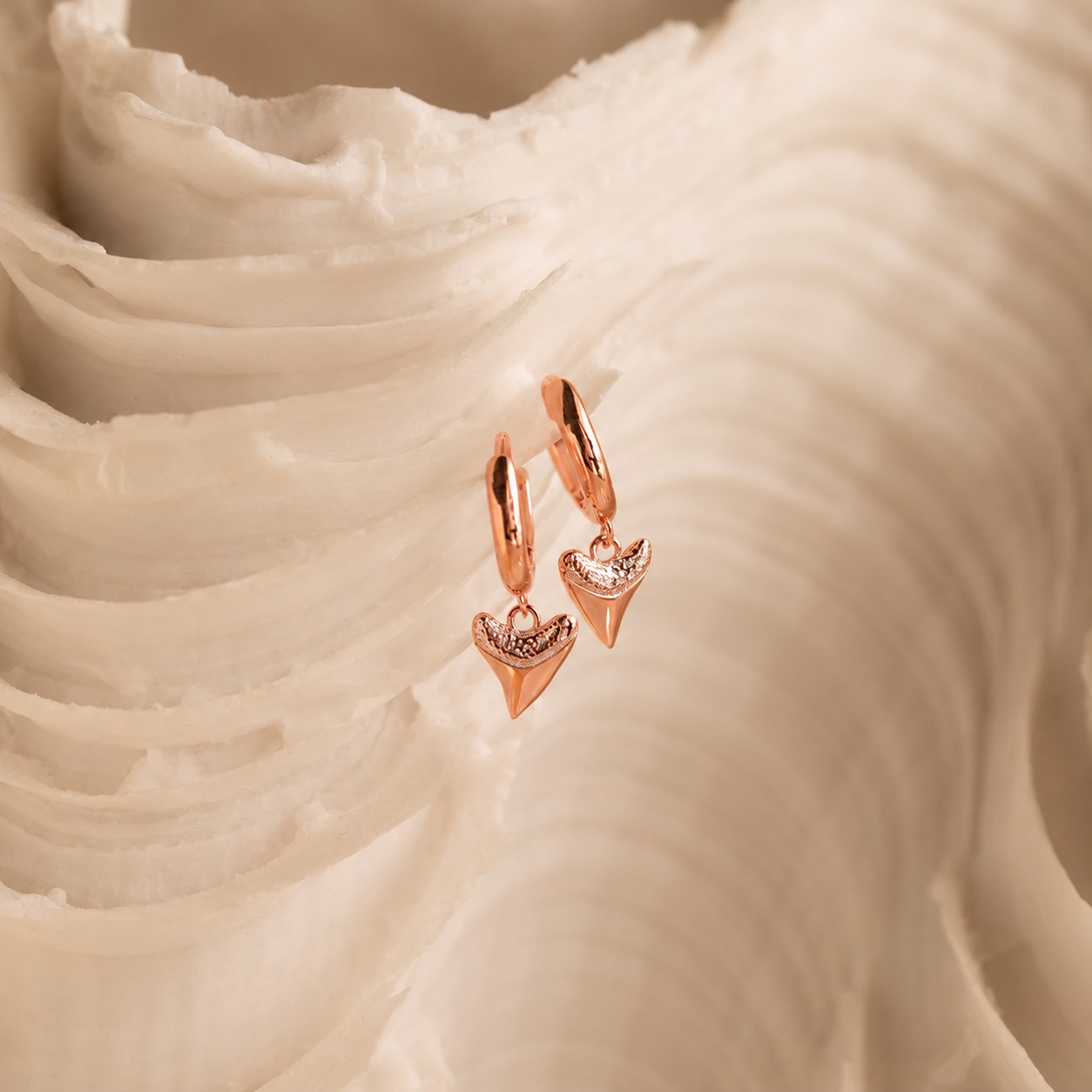 Rose gold earrings with heart-shaped charms on a white fabric background