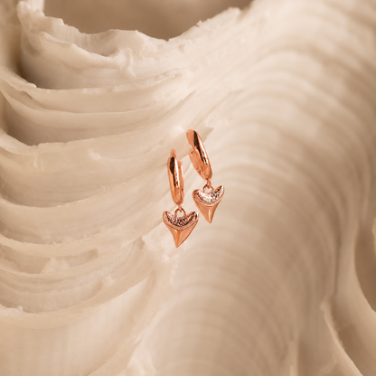 Rose gold earrings with heart-shaped charms on a white fabric background