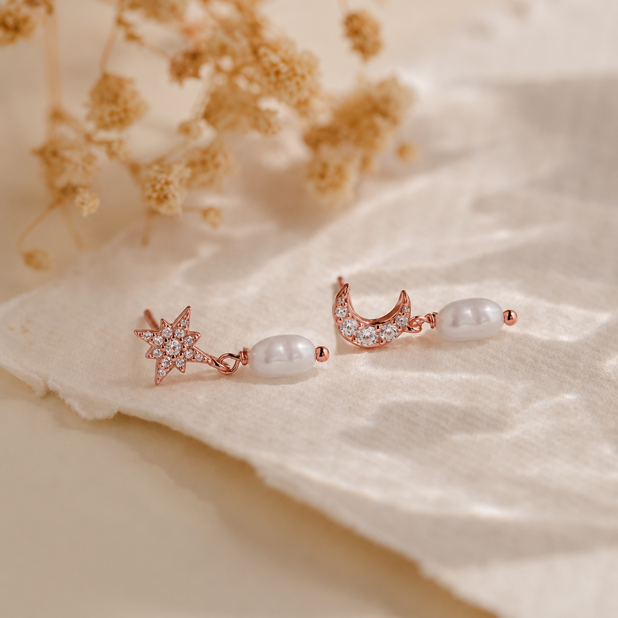 Pair of rose gold earrings with pearls on a soft beige fabric background