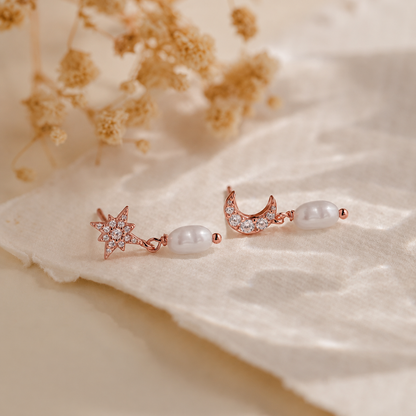 Pair of rose gold earrings with pearls on a soft beige fabric background