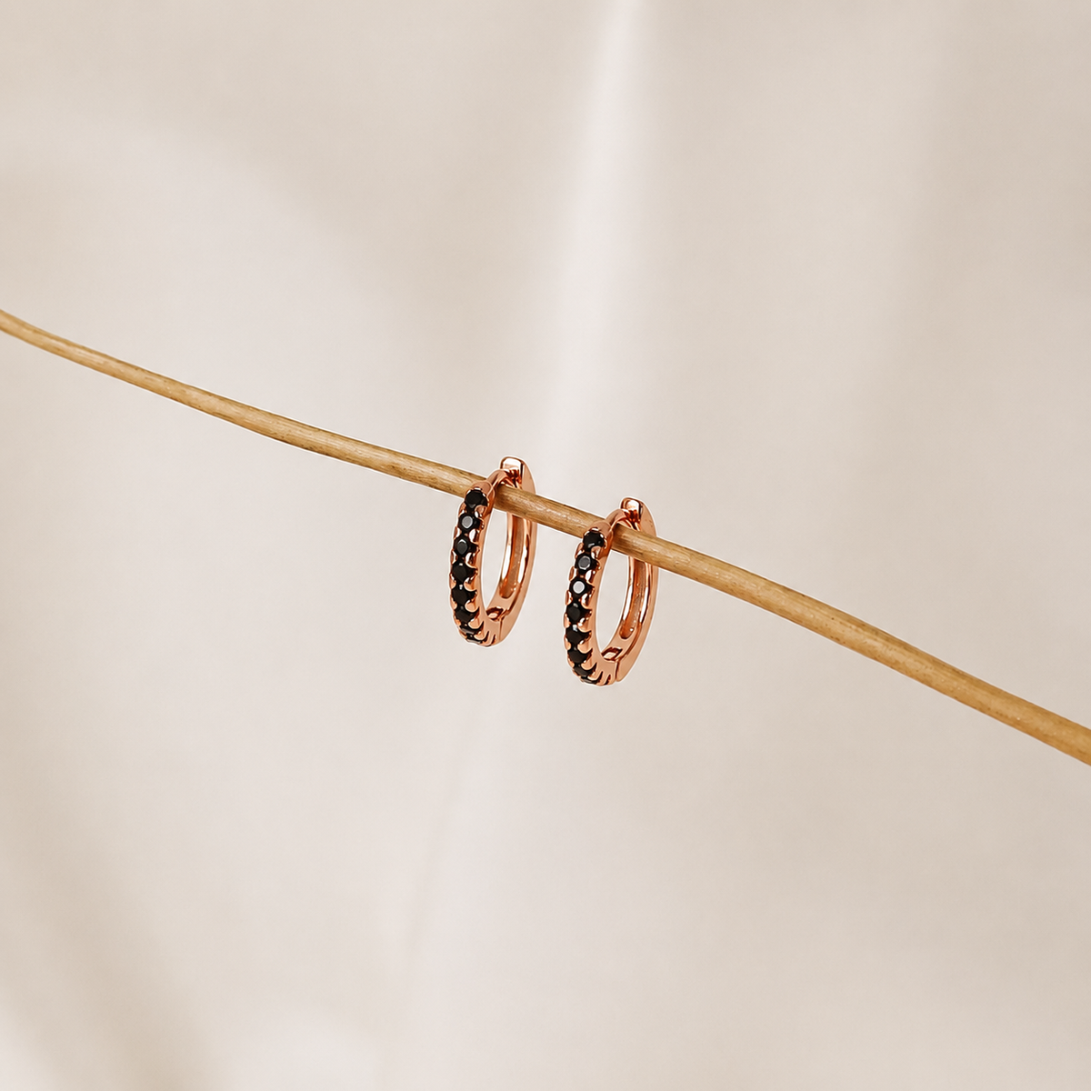 Rose gold hoop earrings with black stones on a beige background