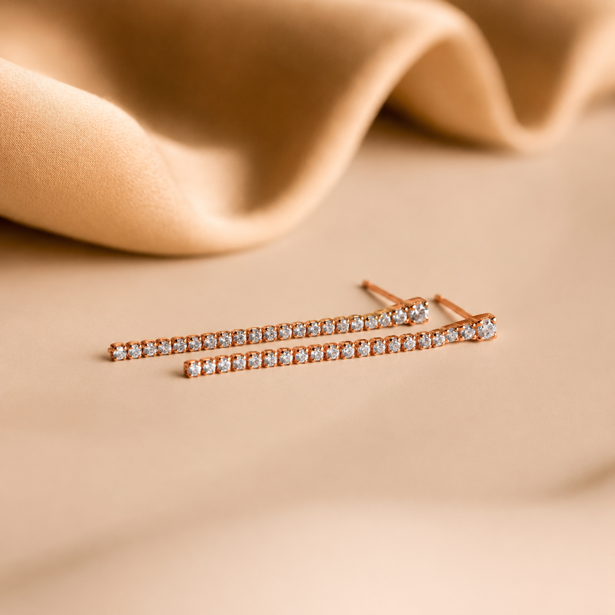 Rose gold earrings with clear stones on a beige fabric background