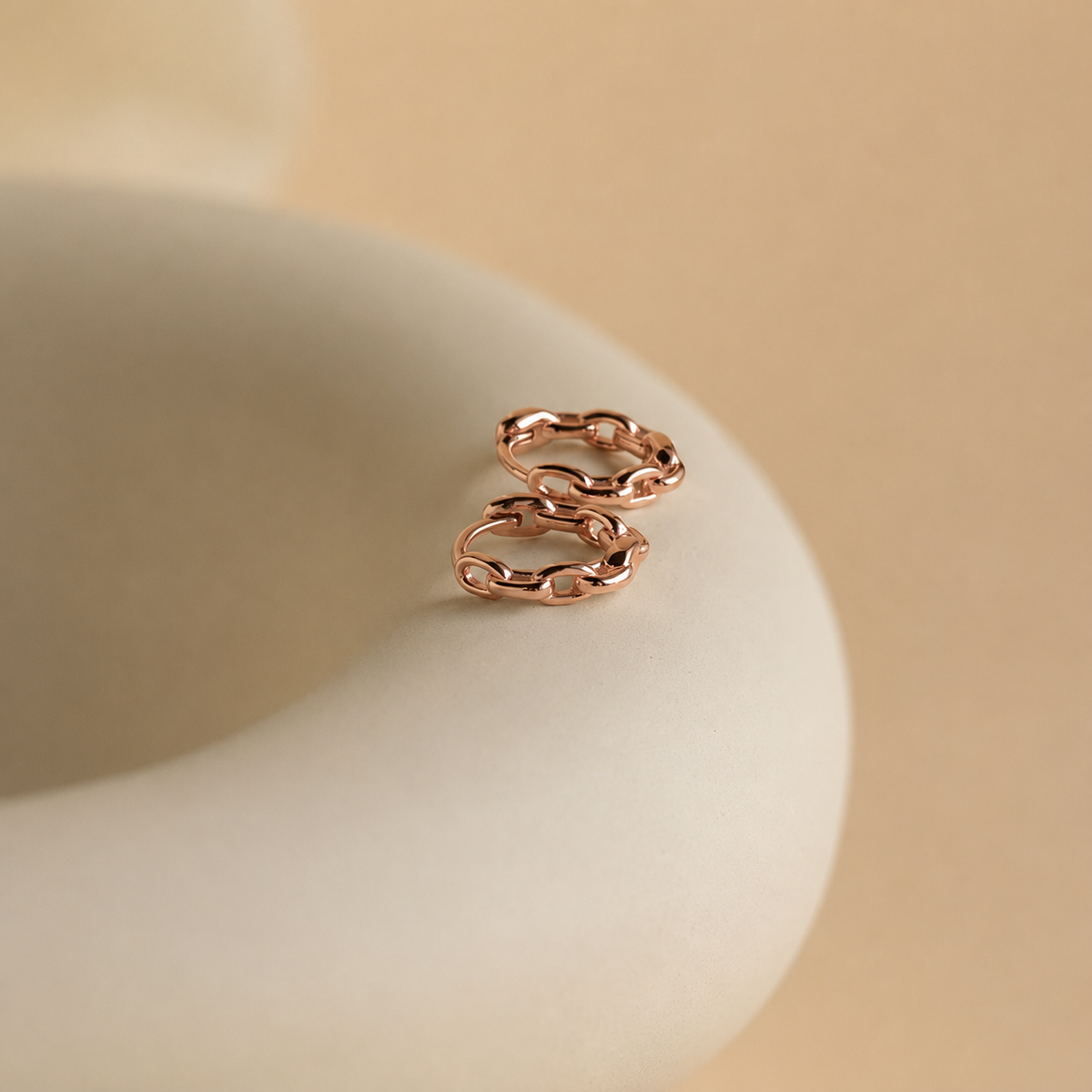 Rose gold chain-style earring on a beige surface with a beige background