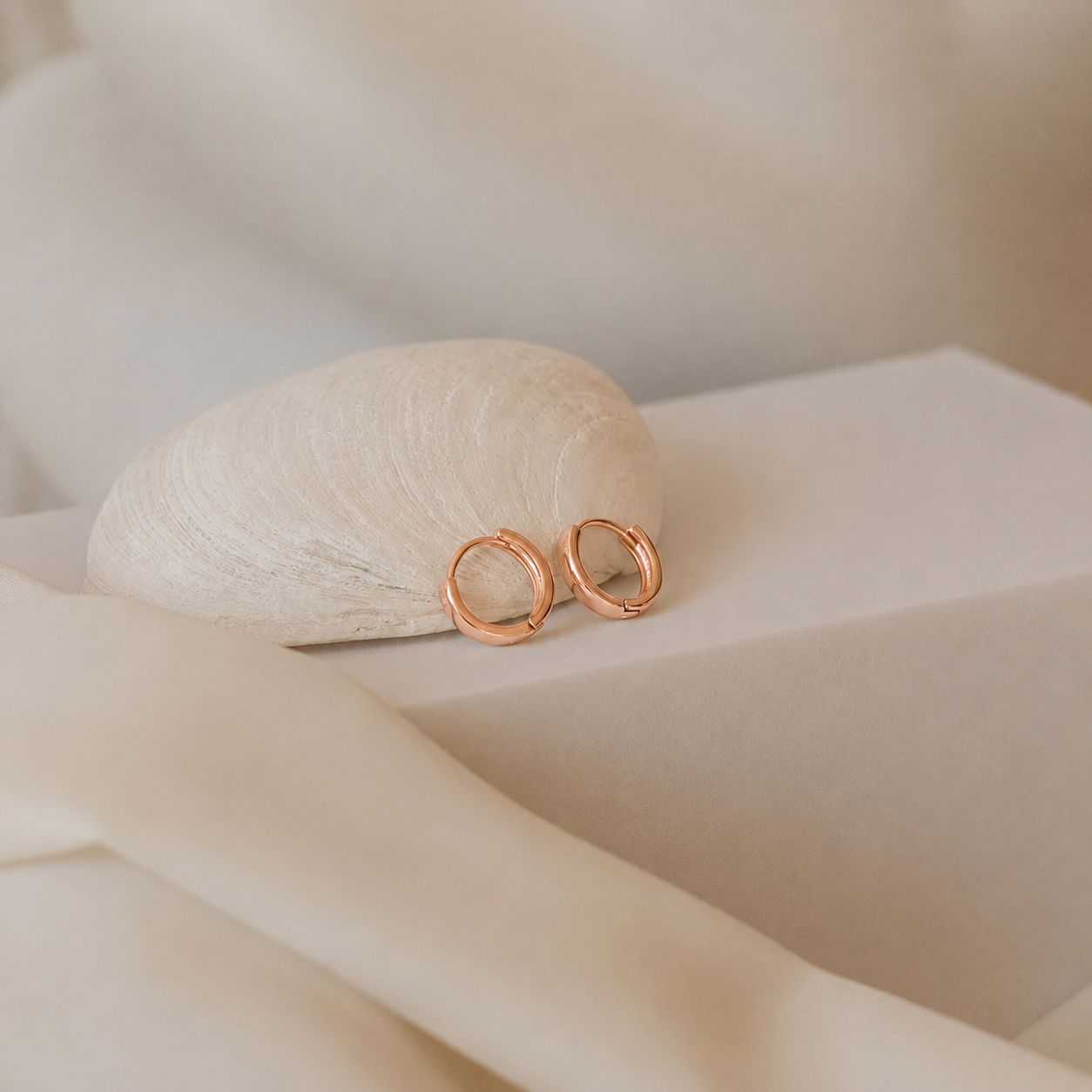 Rose gold earrings on a textured beige surface