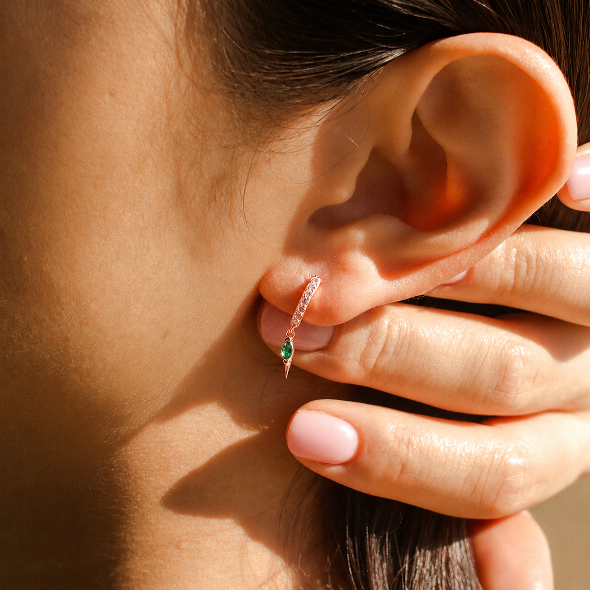 Close-up of an ear with a diamond earring, held by a hand.
