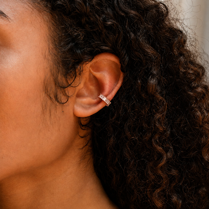 Close-up of an ear wearing a gold earring with a neutral background