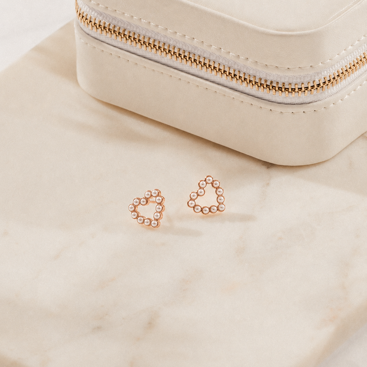 Rose gold hoop earrings on a beige surface with a small pouch in the background