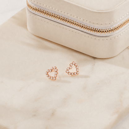 Rose gold hoop earrings on a beige surface with a small pouch in the background