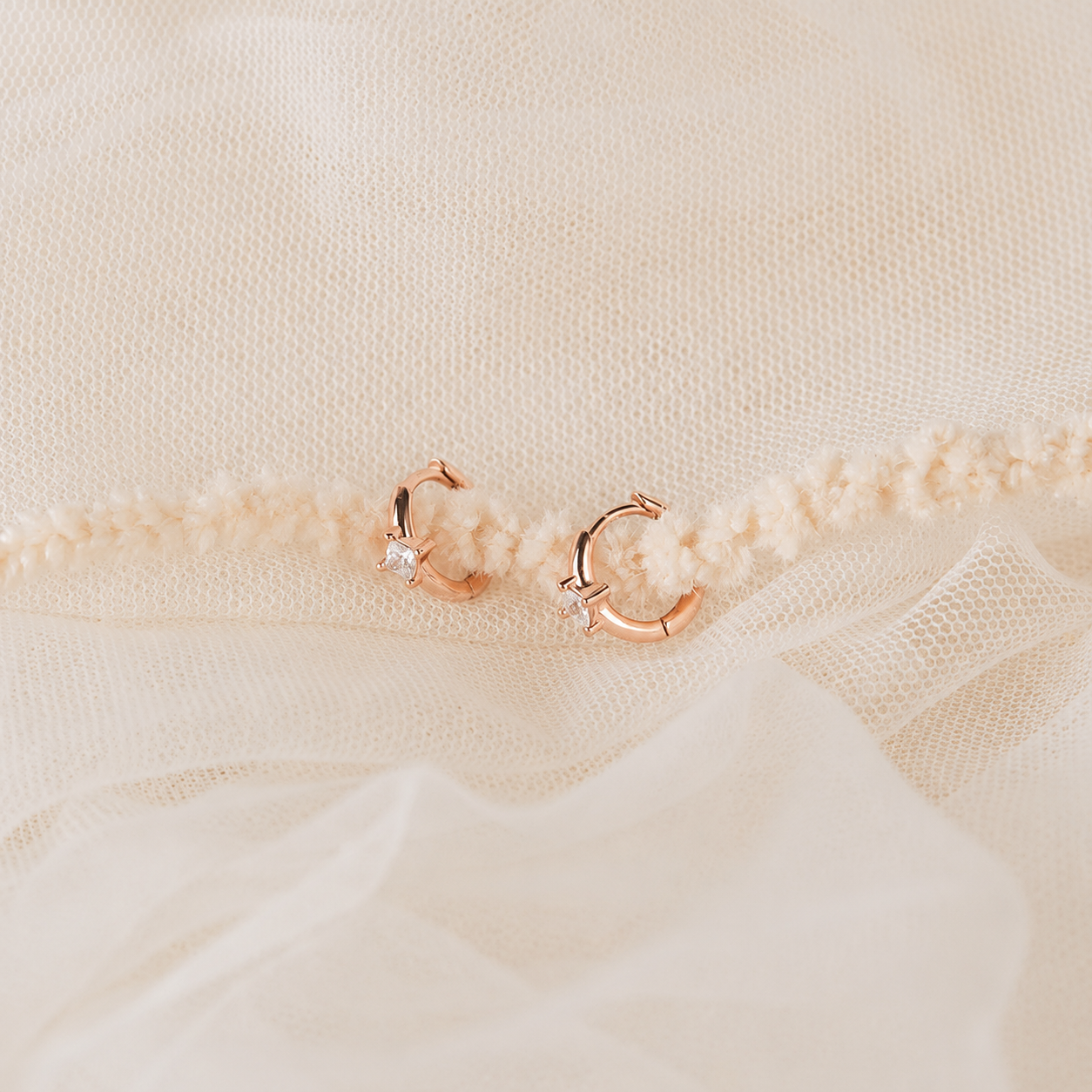 Rose gold hoop earrings on a textured beige fabric background