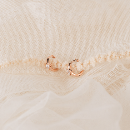 Rose gold hoop earrings on a textured beige fabric background