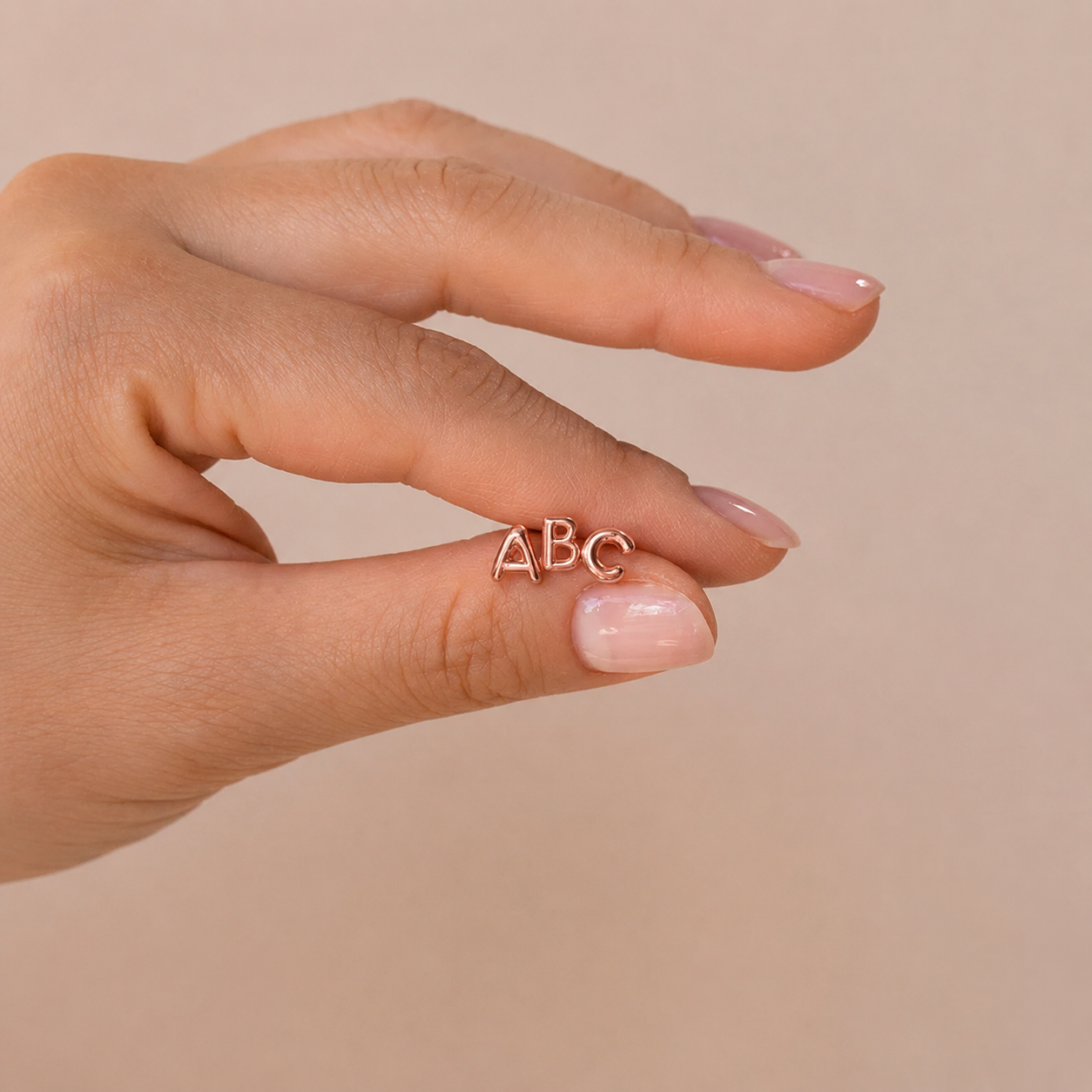 Hand wearing a gold ring with 'ABC' letters on a beige background