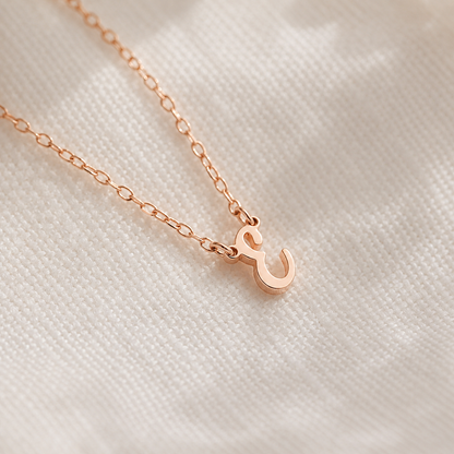Rose gold necklace with a small pendant on a textured beige background