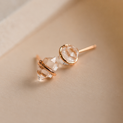 Pair of crystal stud earrings with rose gold accents on a beige background