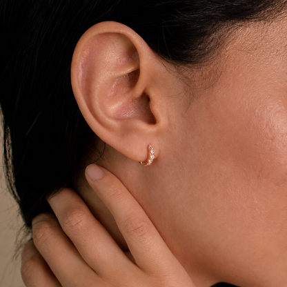 Close-up of an ear with a gold hoop earring and hand touching hair.