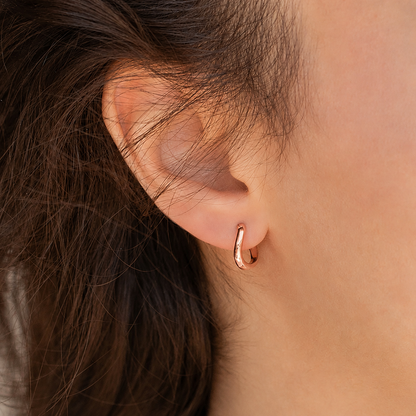 Close-up of an ear wearing a rose gold hoop earring with hair partially covering the side.