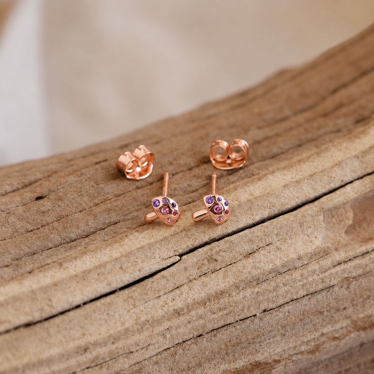 Rose gold earrings with gemstones on a wooden surface