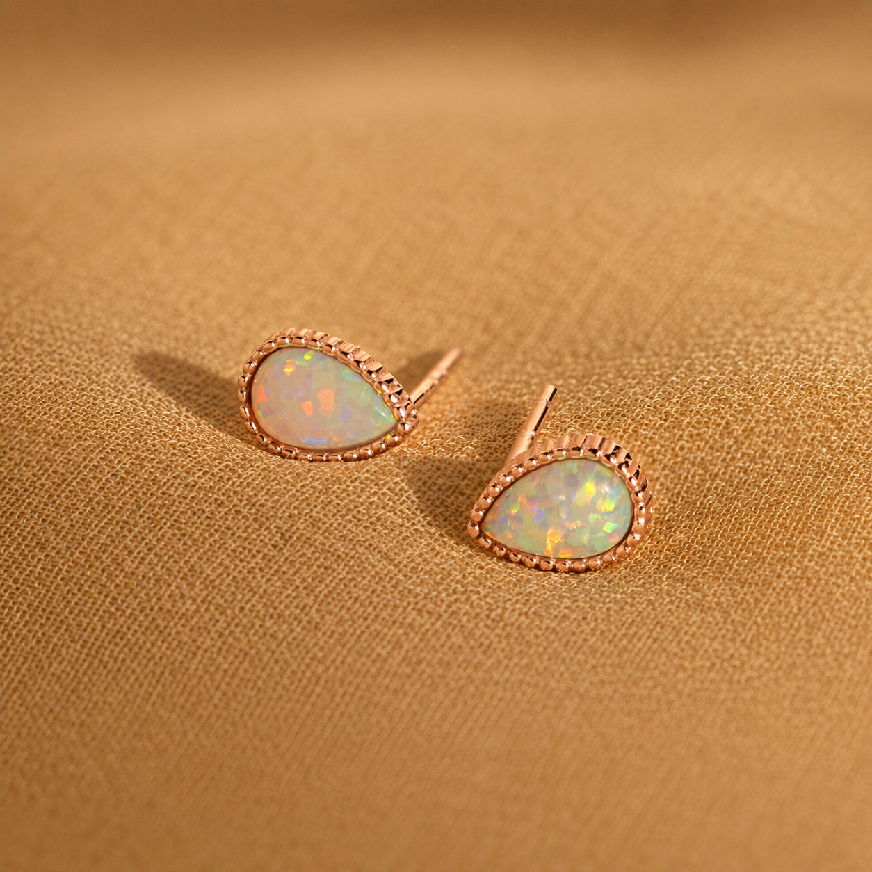 Opal stud earrings with rose gold setting on a beige fabric background