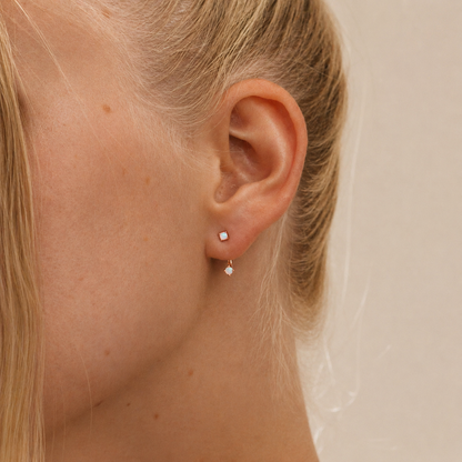 Close-up of a person wearing two small earrings on a neutral background