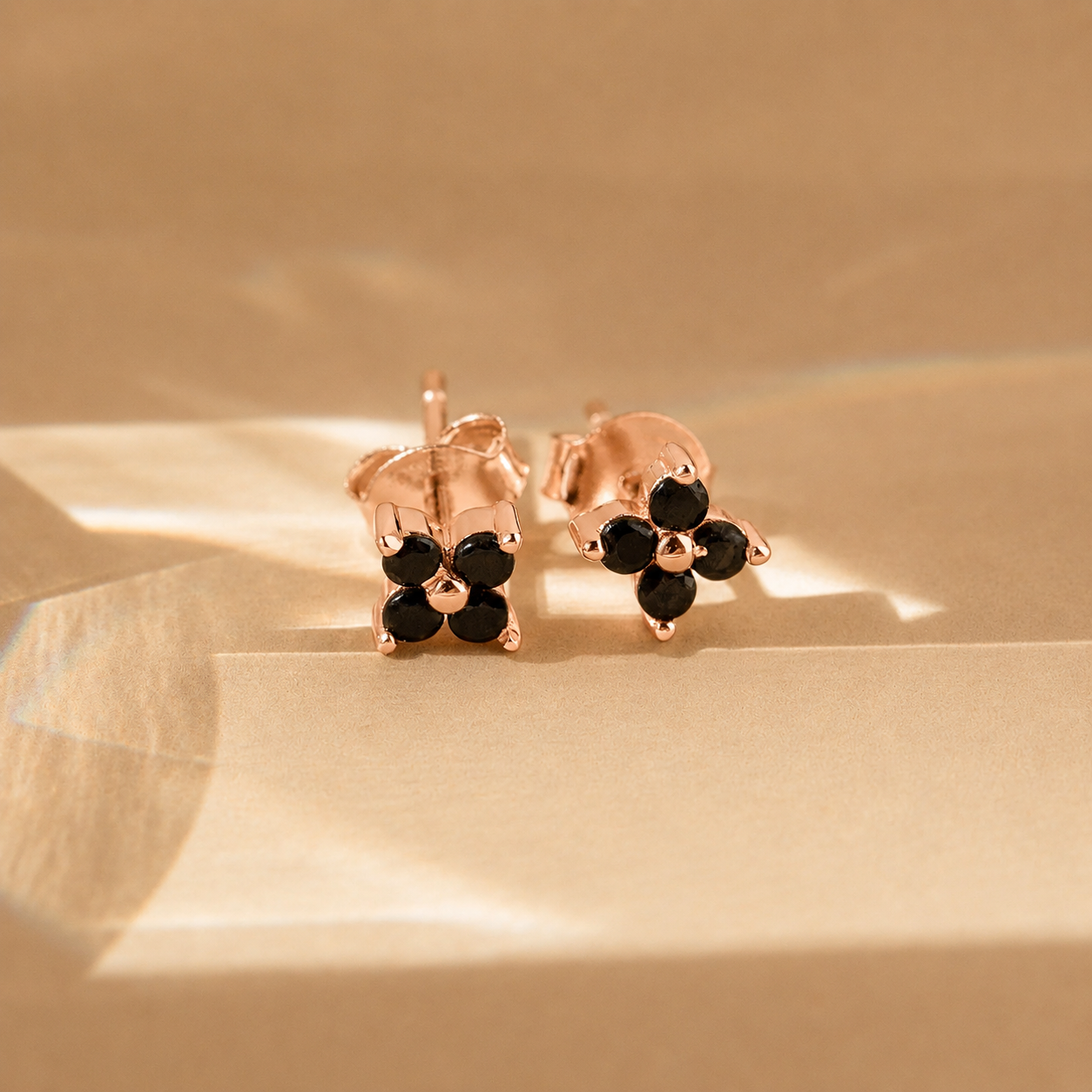 Rose gold earrings with black stones on a beige background