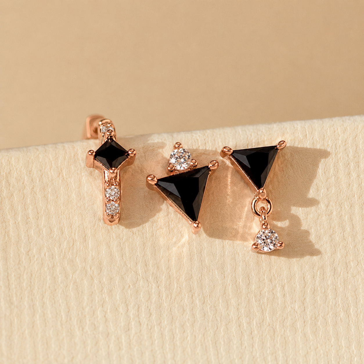 Pair of earrings with black gemstones and rose gold accents on a beige background