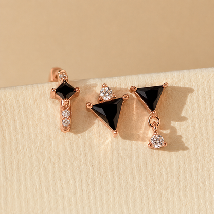 Pair of earrings with black gemstones and rose gold accents on a beige background