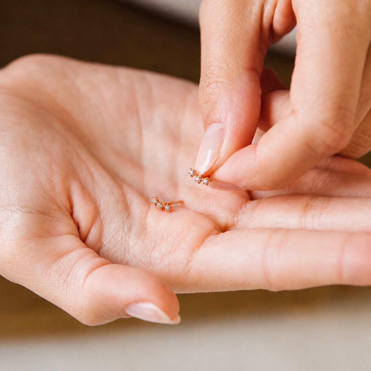 Close-up of hands holding small gold earrings.