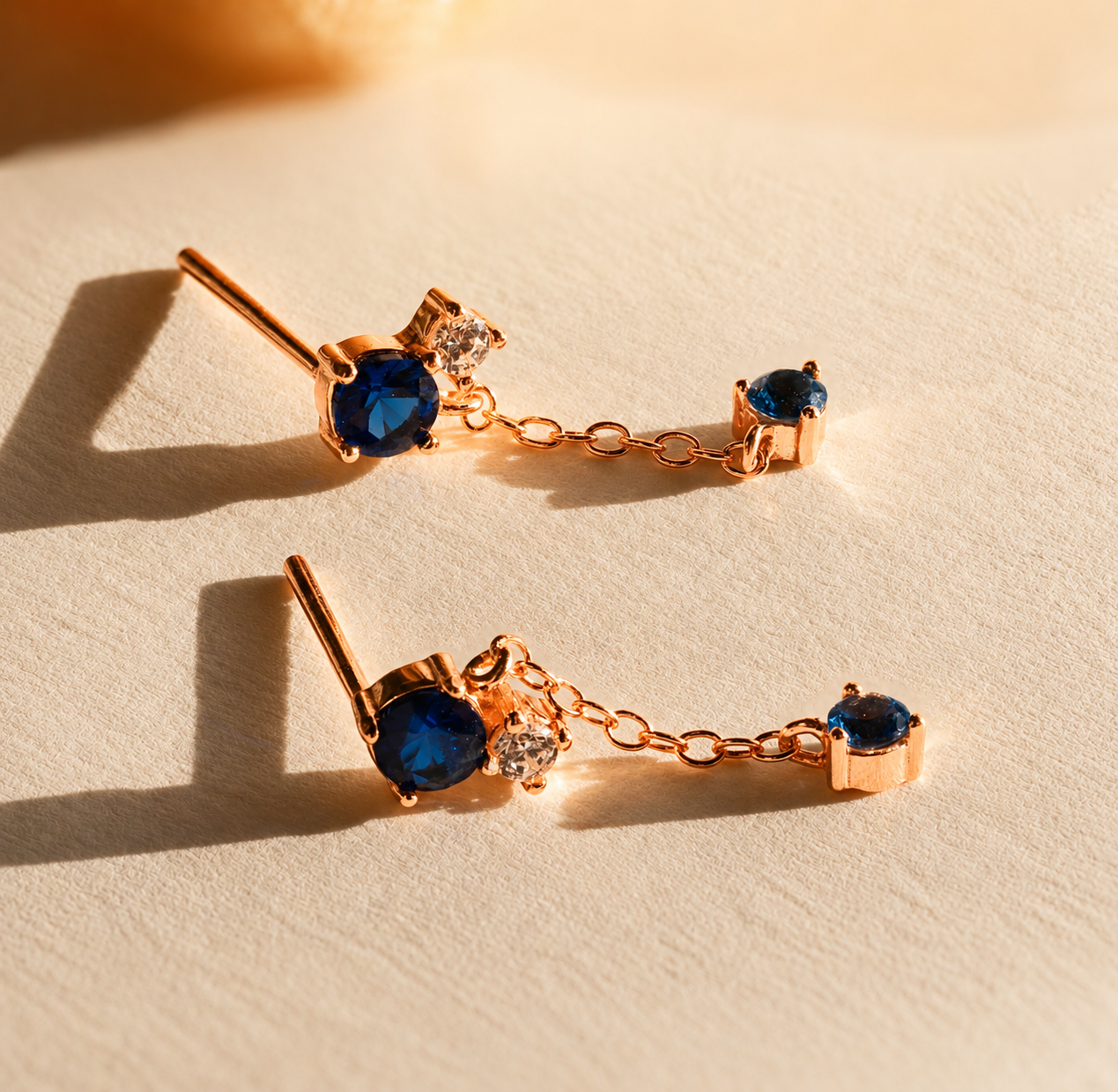 Rose gold earrings with blue gemstones on a beige surface