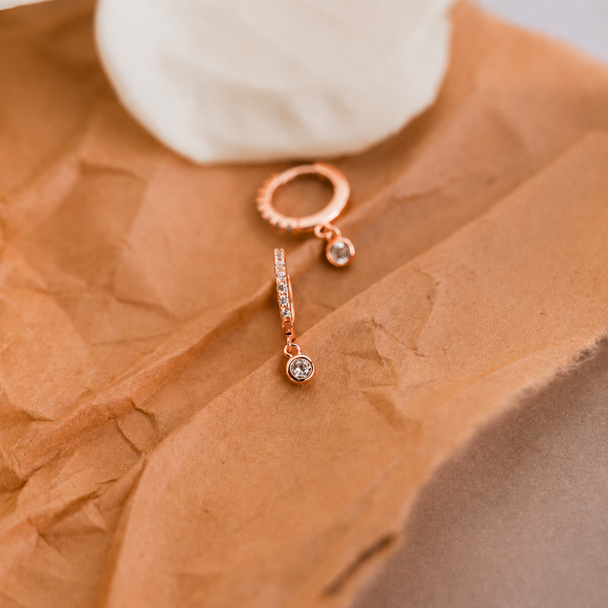 Rose gold earrings with clear gemstones on crumpled brown paper