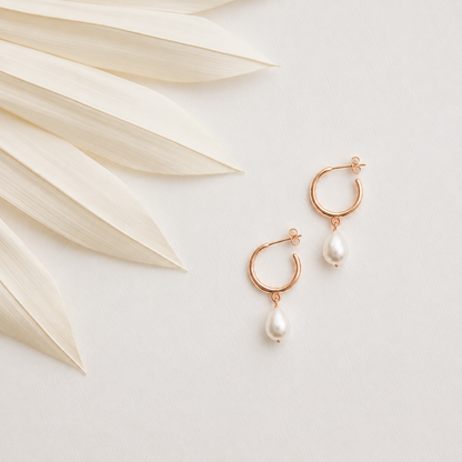 Rose gold hoop earrings with pearl drops on a light background with dried leaves.