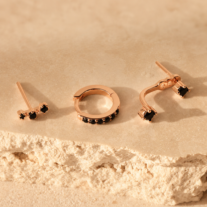 Set of rose gold earrings with black gemstones on a beige stone surface